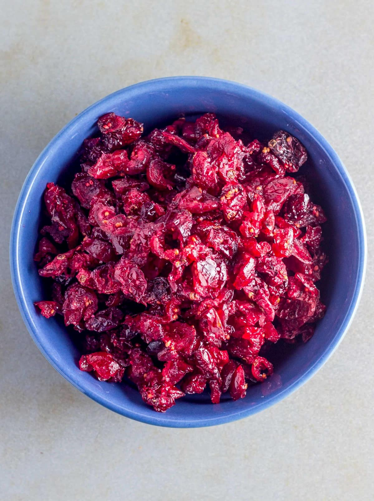 An overhead view of dried cranberries in a small blue bowl. 