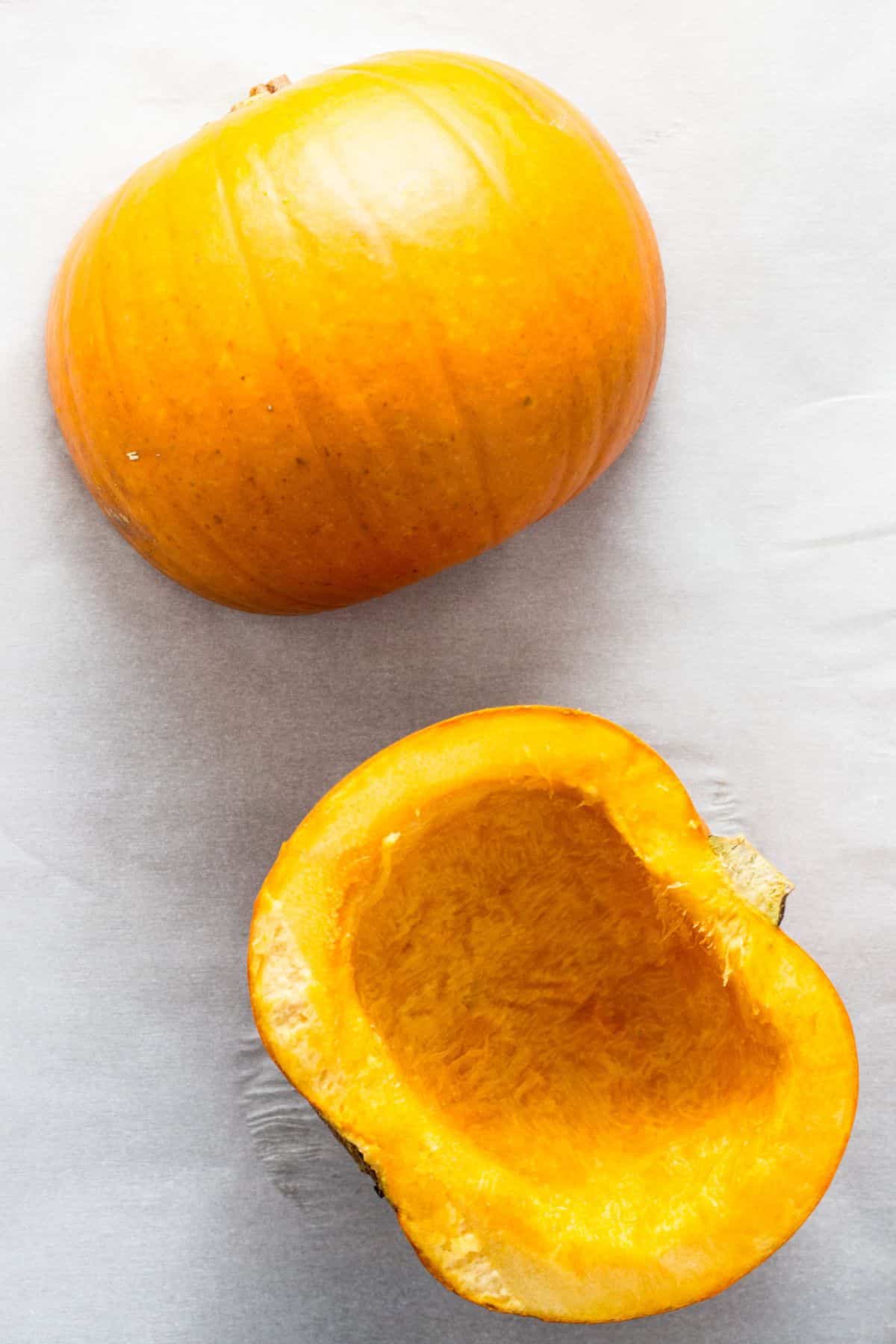 Pumpkin halves on a baking sheet before baking. One half is cut side down while the other half is cut side up.
