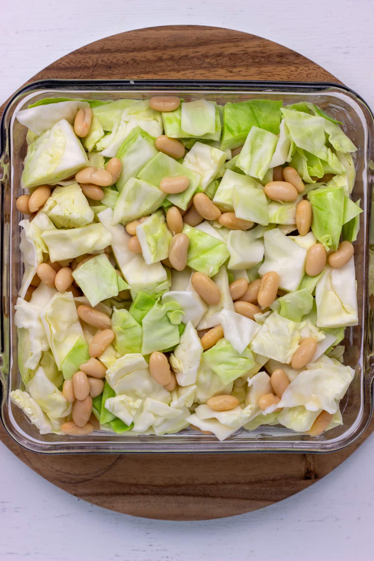 Overhead view of chopped green cabbage and cannellini beans in a casserole dish.