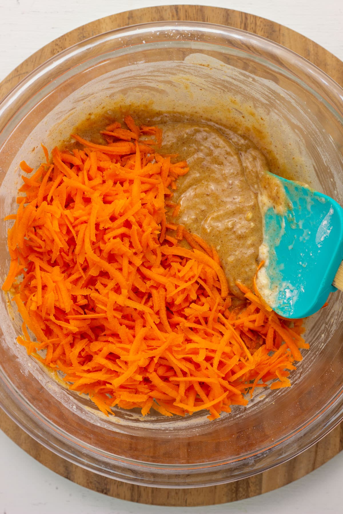Shredded carrots to fold into cake batter with a spatula. The bowl sits on a round wooden board.