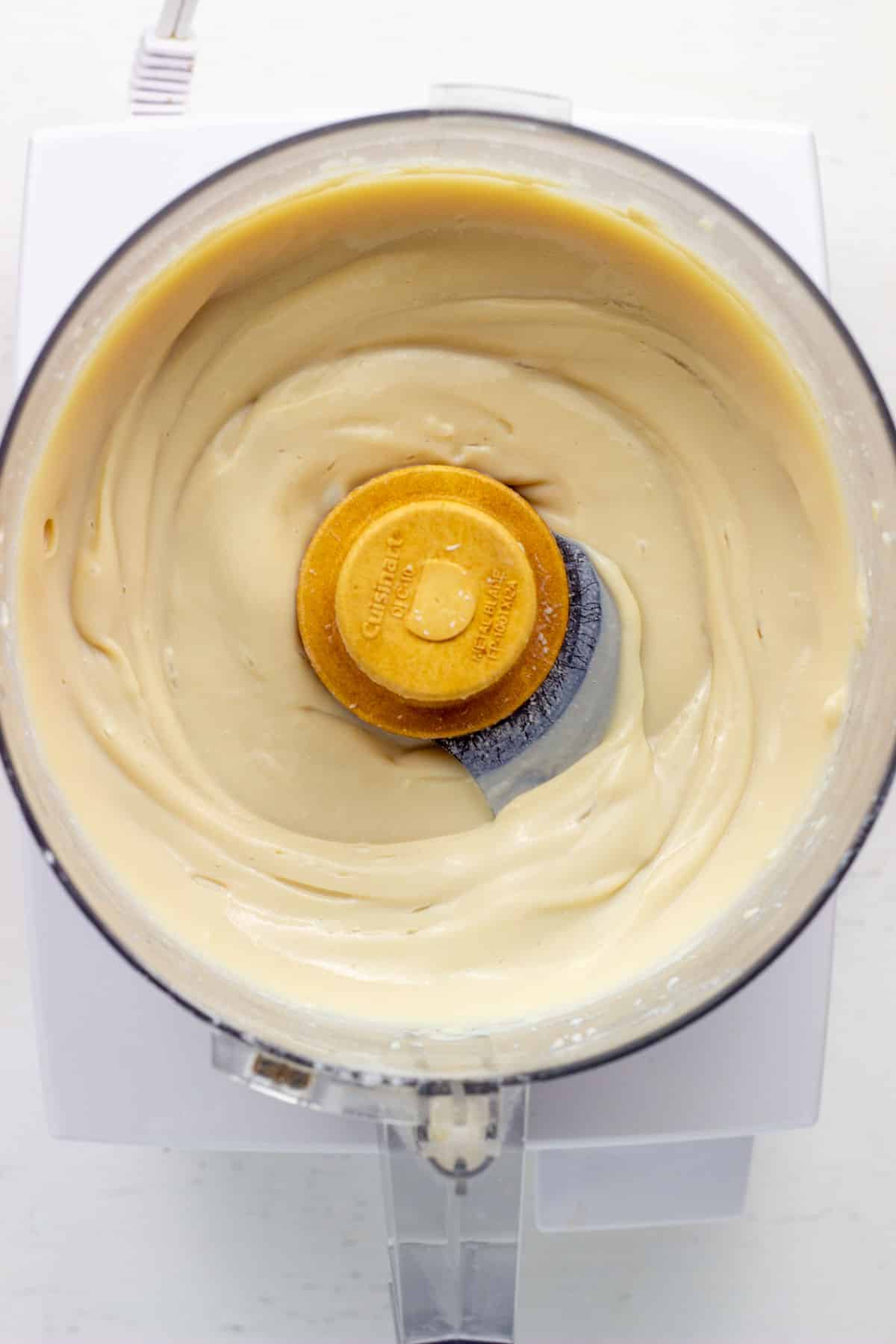 Vegan cheesecake in the bowl of a food processor. The cheesecake if made from tofu and a few other ingredients blended until smooth.