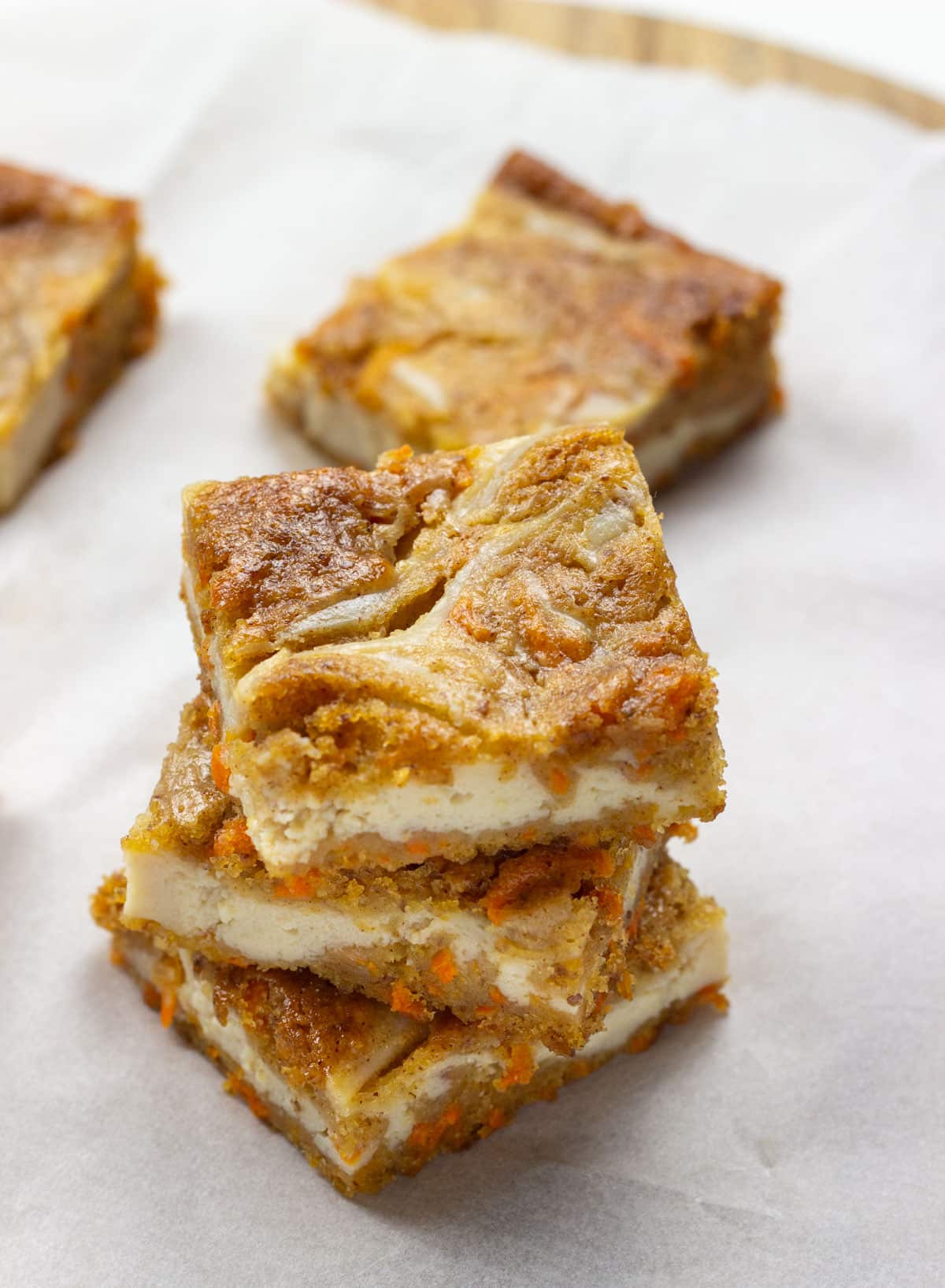 Three Vegan Carrot Cake Cheesecake Bars stacked. There are more bars partially visible in the background.