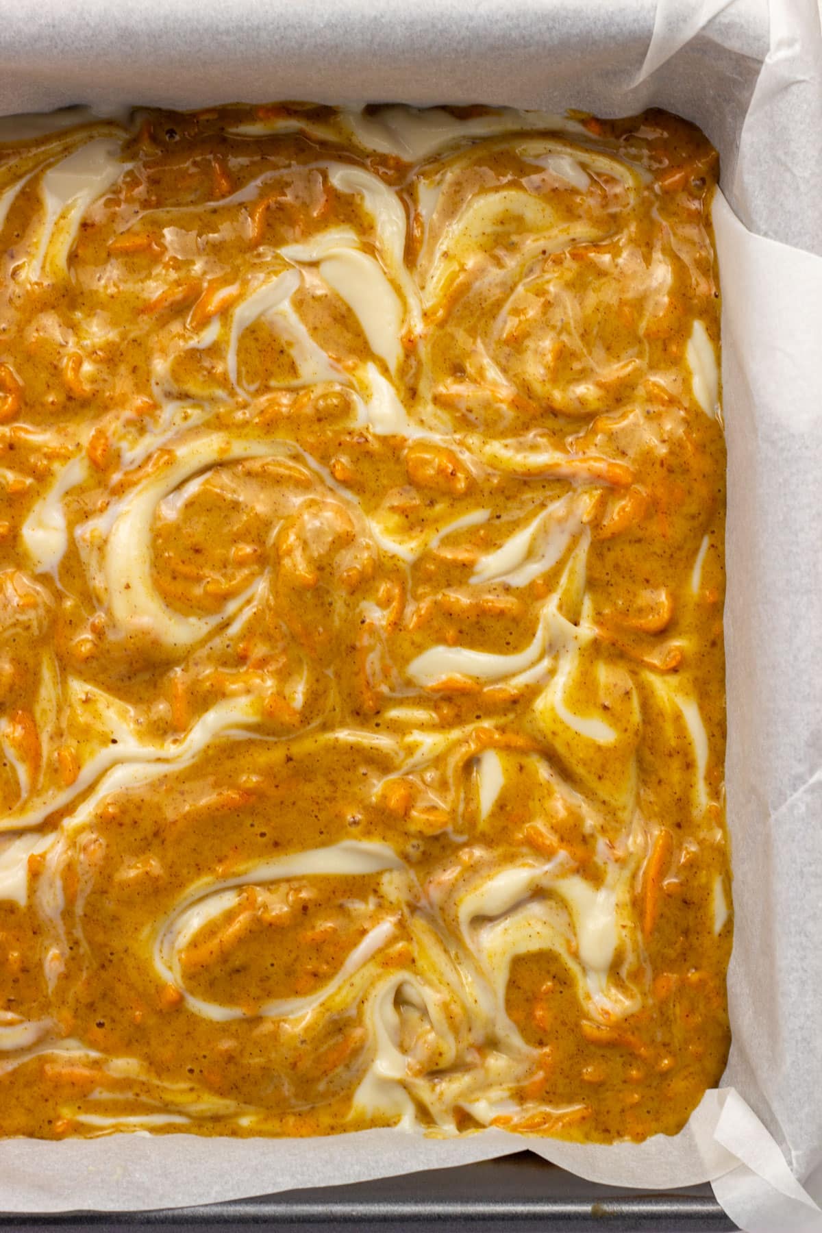 Close up view of Vegan Carrot Cake Cheesecake Bars before baking. Cheesecake is swirled throughout the cake batter.