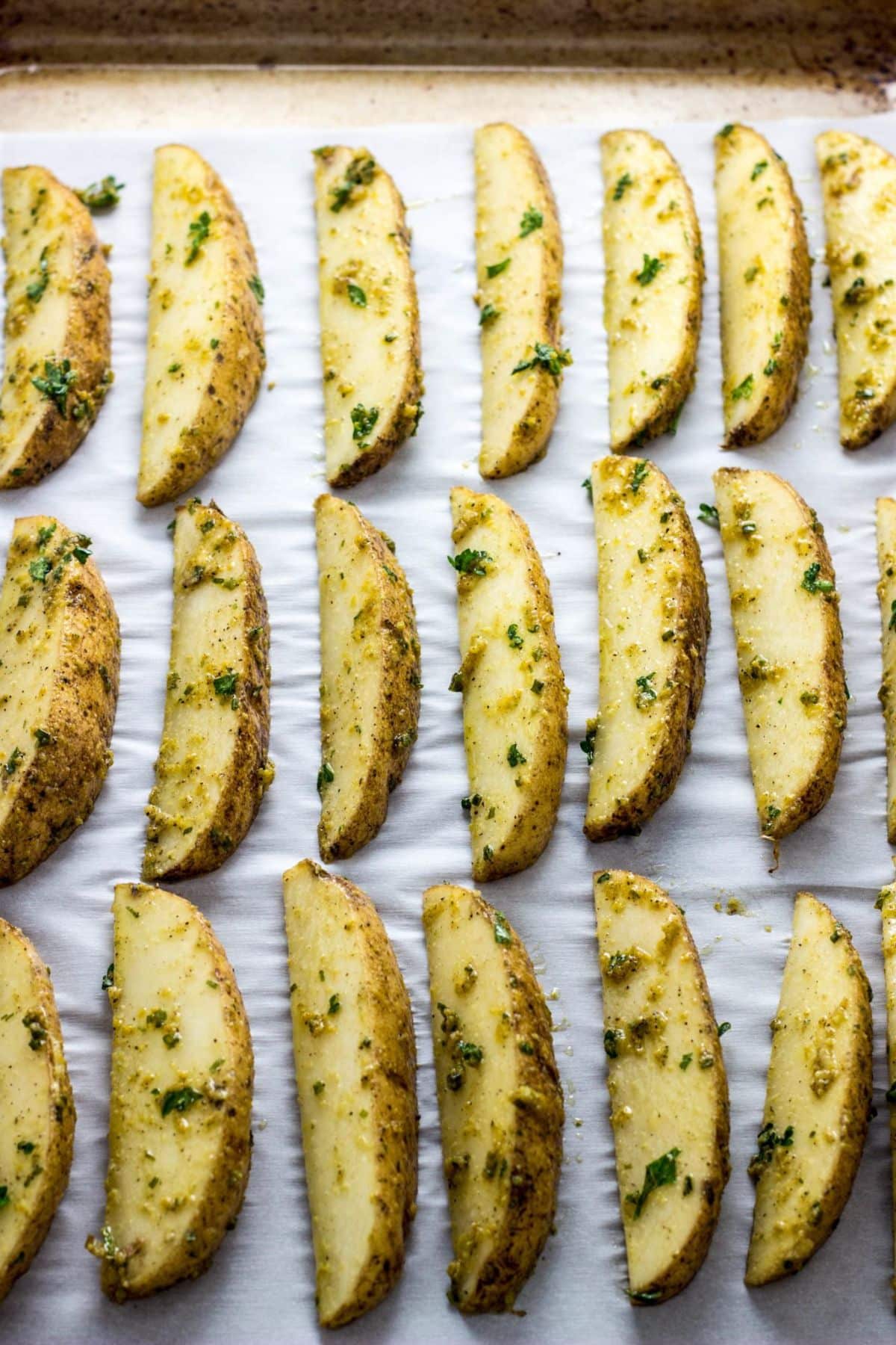 Potato Wedges on a baking sheet before baking. The wedges are coated in a herb, oil and nutritional yeast mixture.