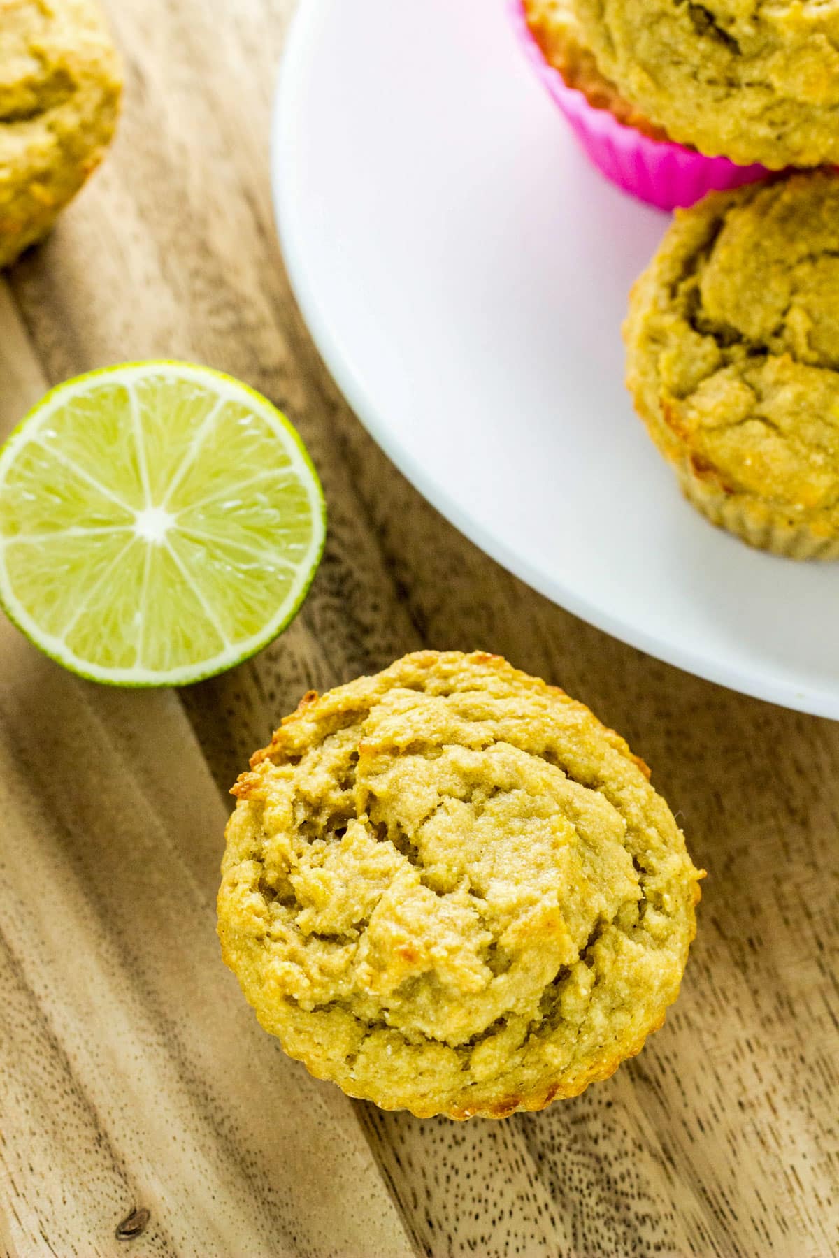 Overhead view of a Vegan Lime Avocado Muffin on a wooden on a wooden board. Other muffins and half of a lime are also visible.