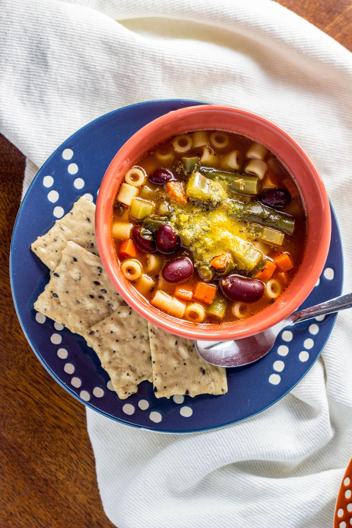 Overhead view of a bowl of Vegan Minestrone Soup. The bowl sits on a small plate with crackers in the bottom right of the plate.