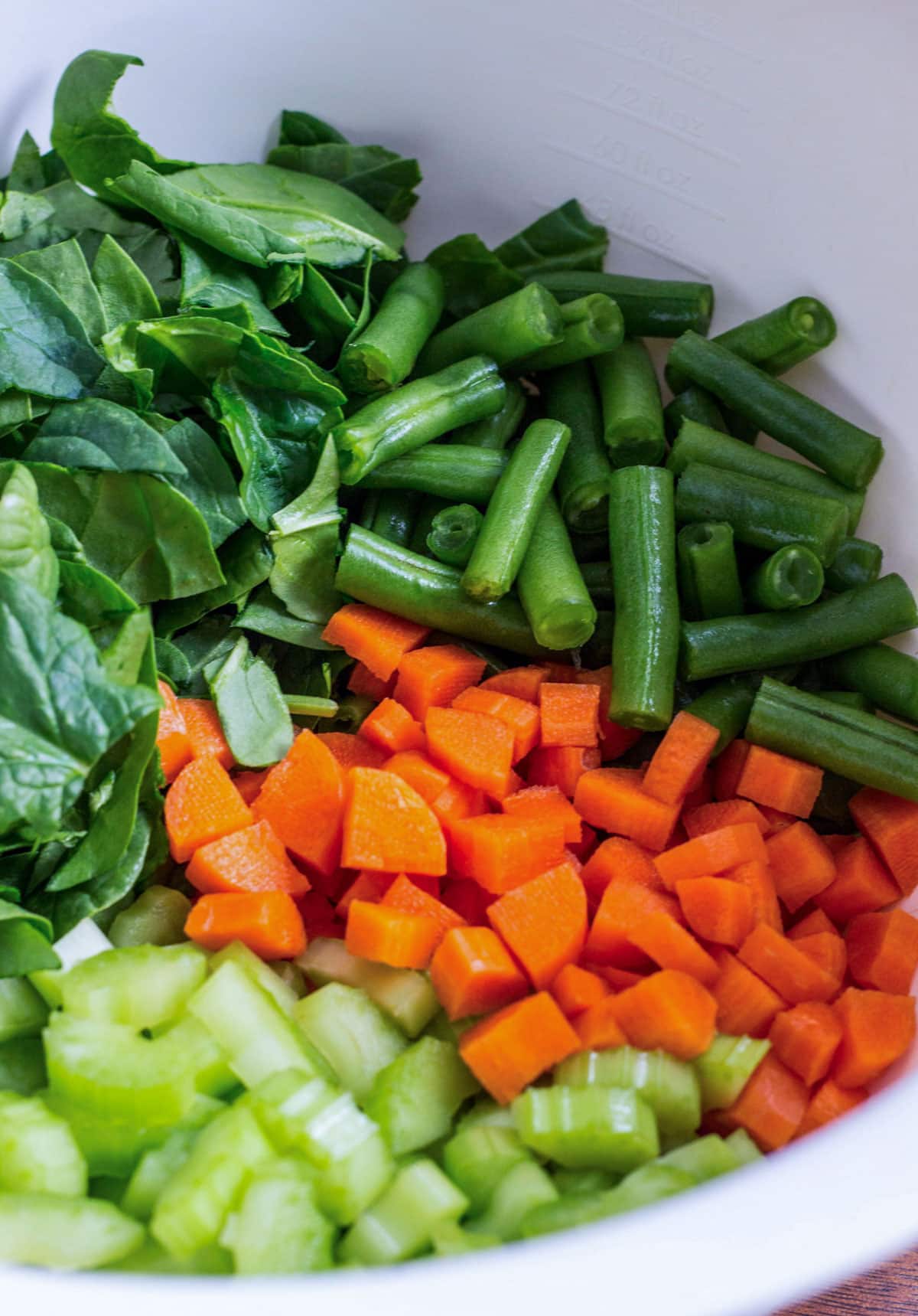 Close up of a bowl filled with chopped celery, chopped carrots, green beans and spinach.