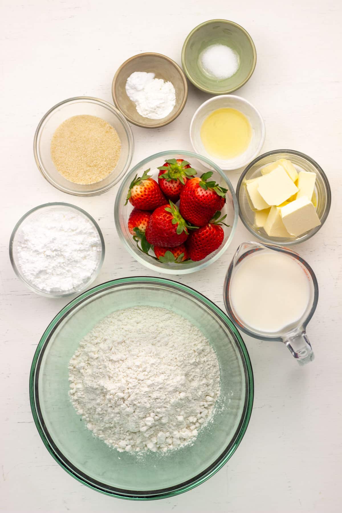 Ingredients for Vegan Strawberry Butter Swim Biscuits. There are bowls of flour, strawberries, confectioner's sugar, non dairy butter, non dairy milk, sugar, apple cider vinegar, salt, baking powder and baking soda.