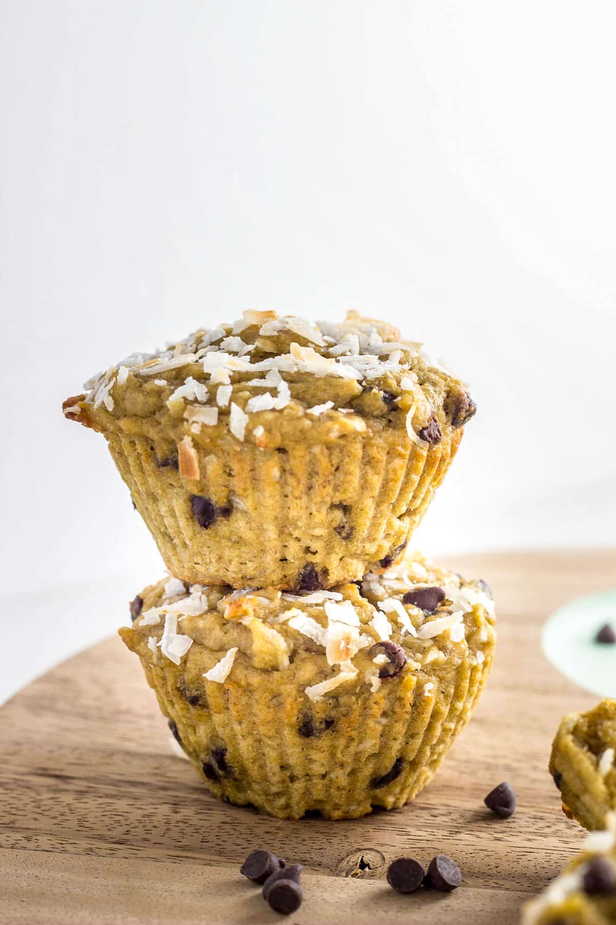Close up side view of two Coconut Chocolate Chips Muffins stacked on a wooden cutting board.