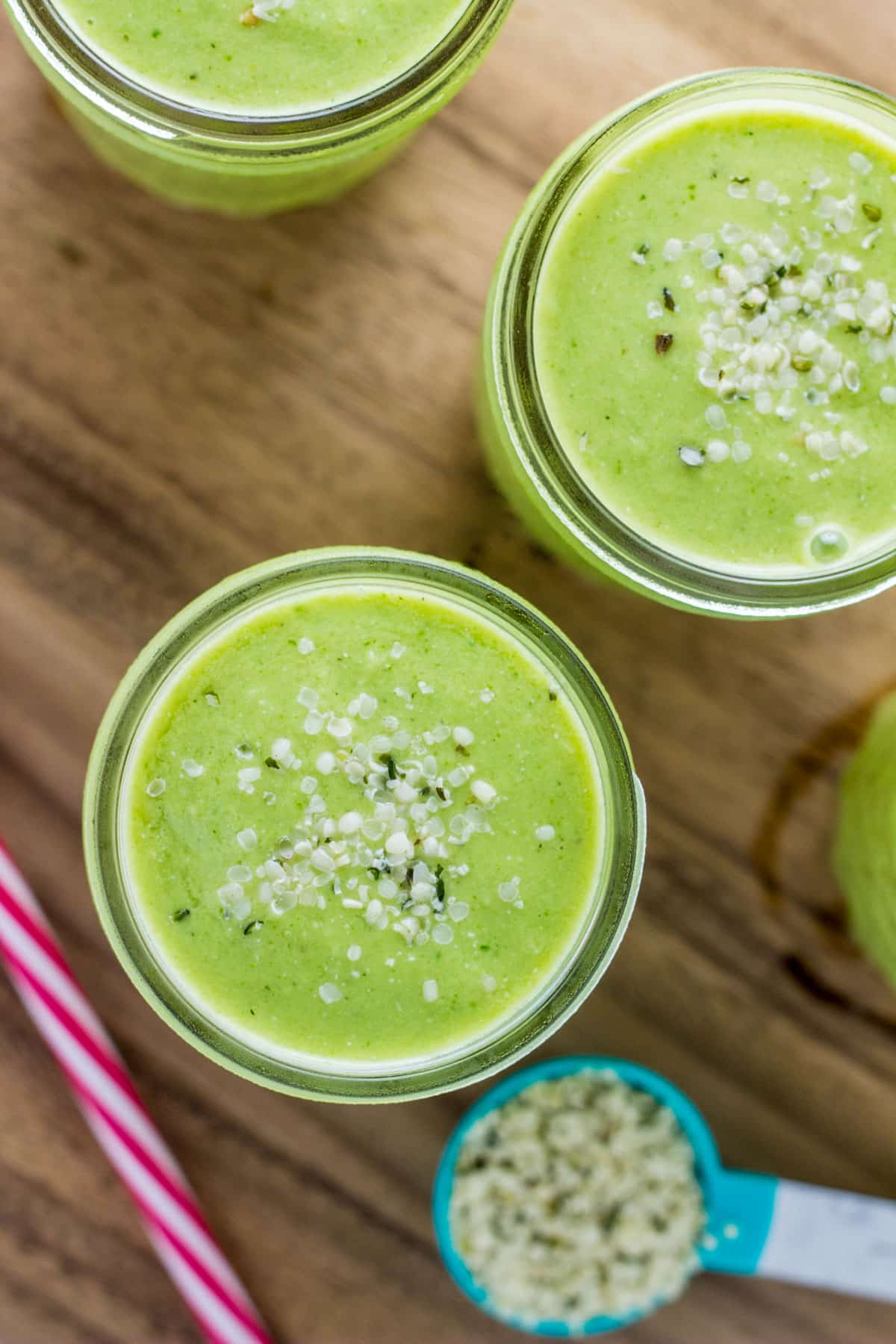 Overhead close up view of glasses of Kid Friendly Green Smoothie. There is a spoon of hemp seeds visible in the lower right corner of frame.