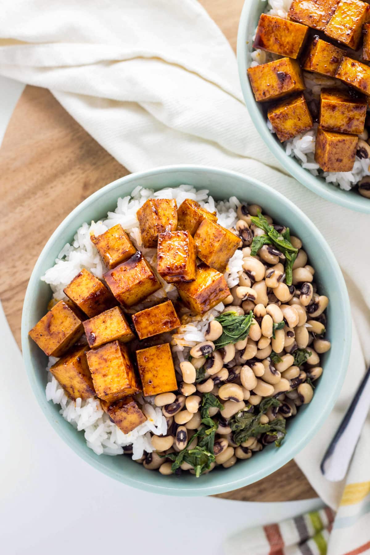Overhead view of Smoky Tofu Black-Eyed Pea Bowls. The bowl has a sauced tofu over rice and black-eyed peas mixed with sautéed greens.