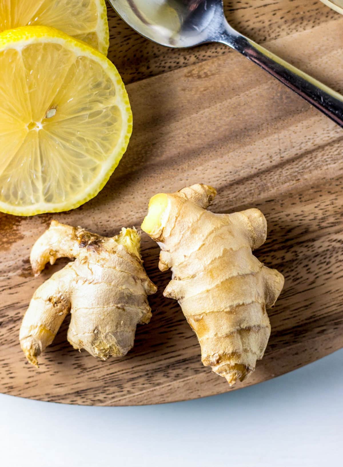 Fresh ginger root on a wooden board with lemon slices in the upper left corner.