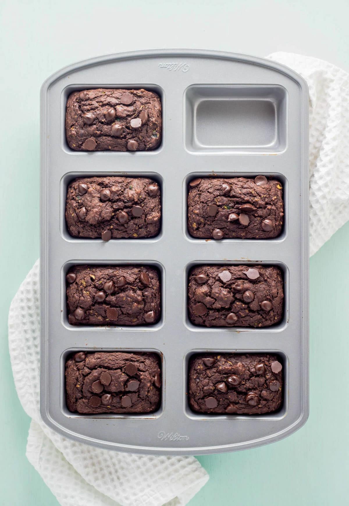 Overhead shot of Chocolate Zucchini Bread Mini Loaves in a loaf pan. A pan sits on a white textured kitchen towel.