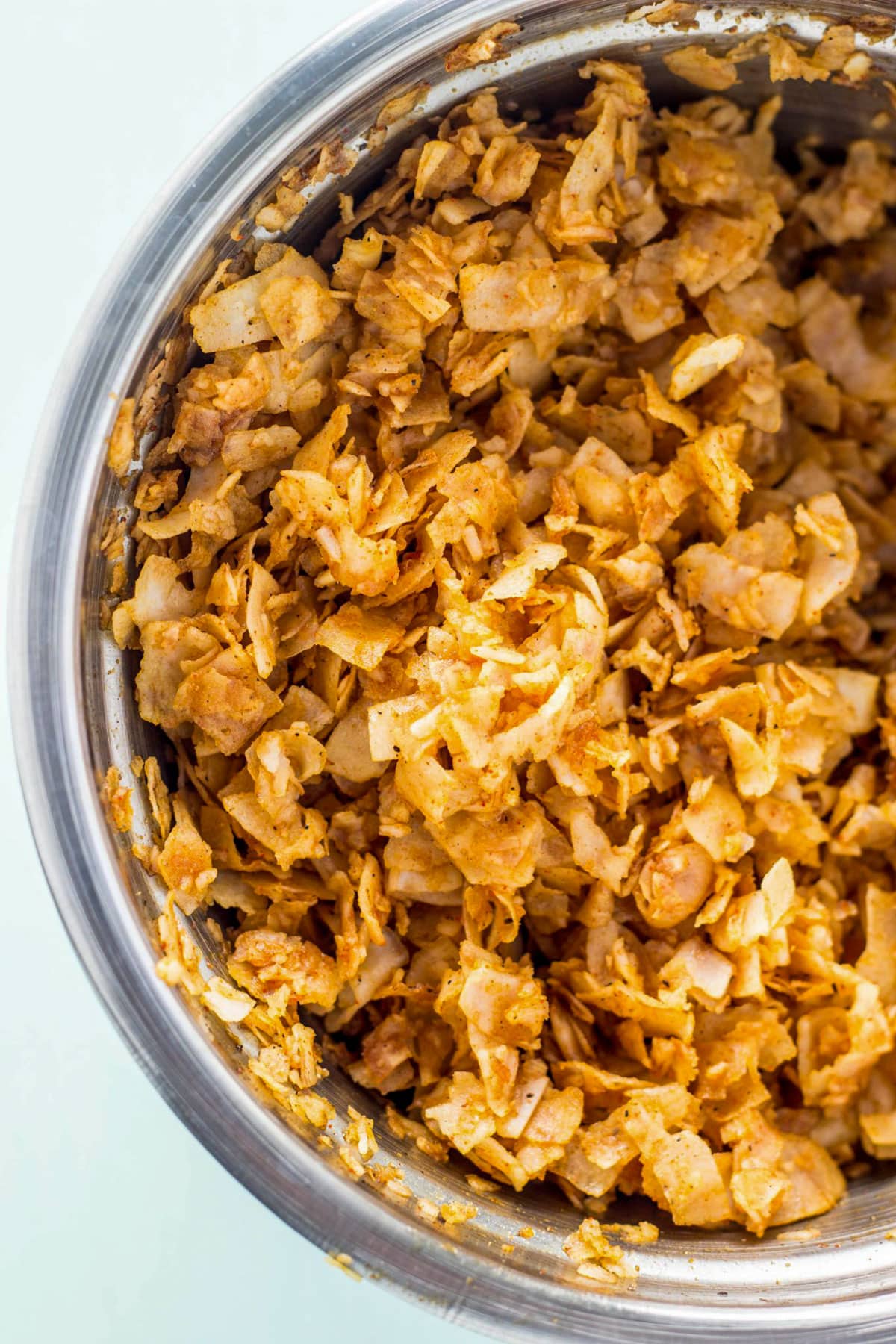 Coconut seasoned with spices in a metal bowl. The coconut is baked to make coconut bacon, a vegan alternative to conventional bacon.