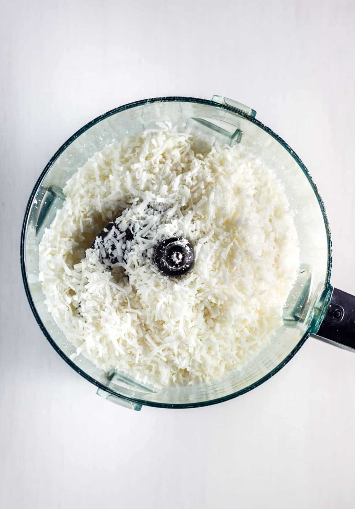Shredded coconut in the bowl of a food processor.