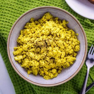 Top view close up of Basic Tofu Scramble in a bowl sitting on a green towel with a fork to the side.