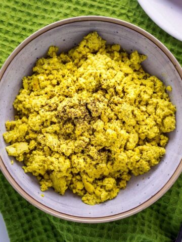 Top view close up of Basic Tofu Scramble in a bowl sitting on a green towel with a fork to the side.