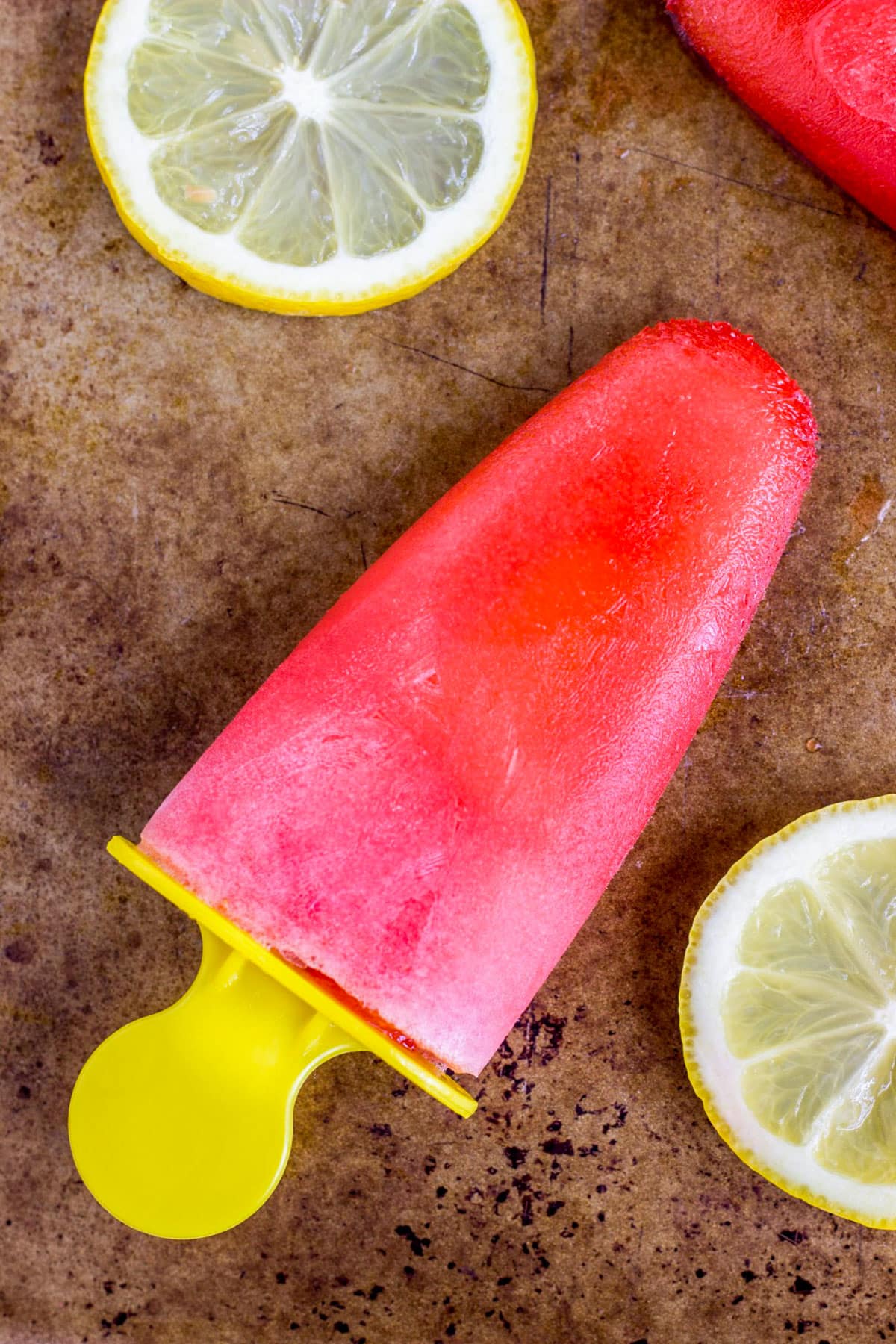 Close up of a Strawberry Lemonade Popsicle on laying a baking sheet with lemon slices on the side.