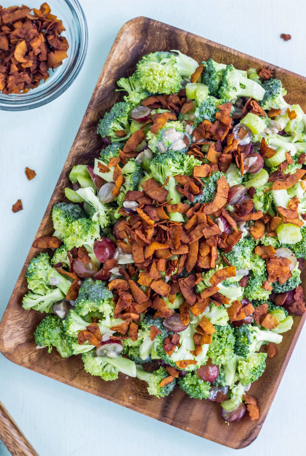 Vegan Broccoli Grape Salad on a rectangular wooden plate. Coconut bacon is sprinkled over the top of the salad.