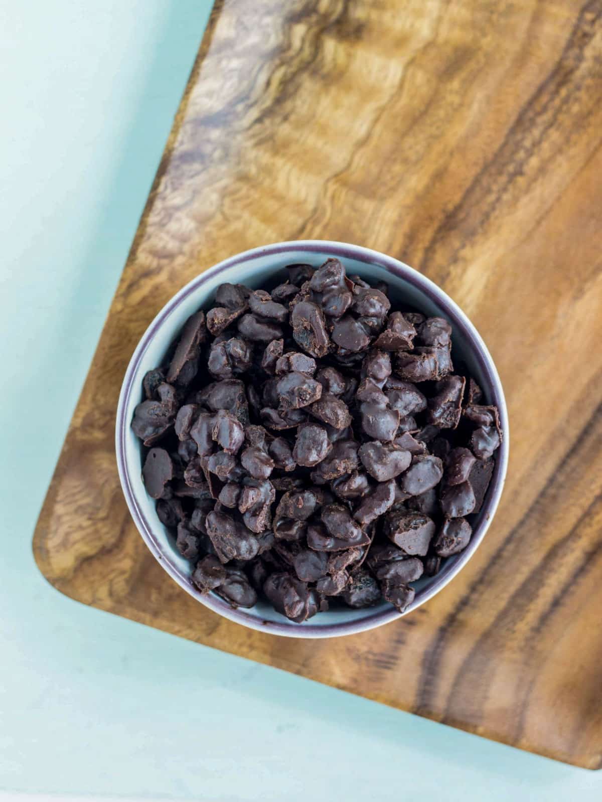 A small bowl of Vegan Chocolate Covered Raisins on a wooden board.
