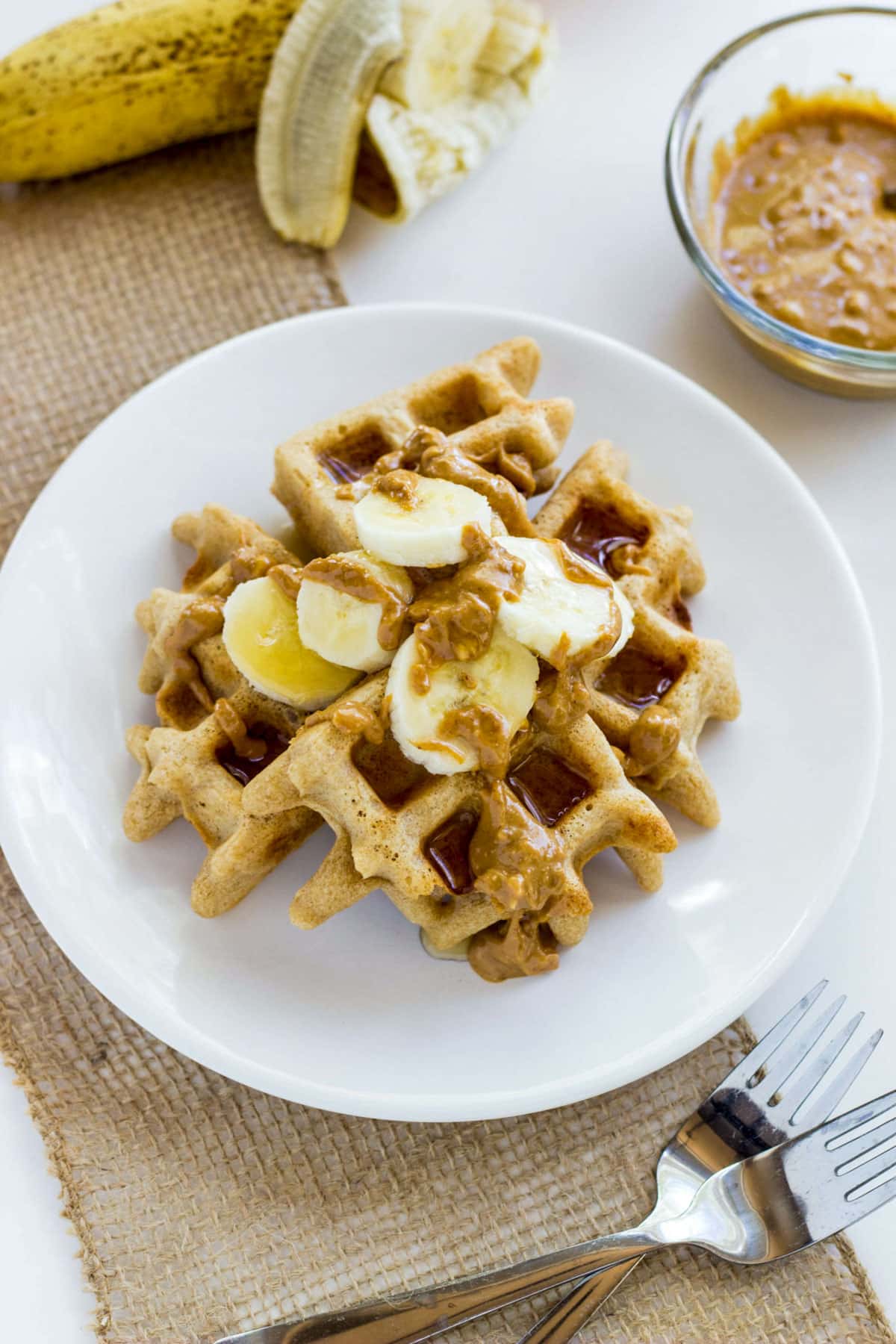 Vegan Whole Wheat Waffles topped with banana slices, peanut butter and maple syrup.