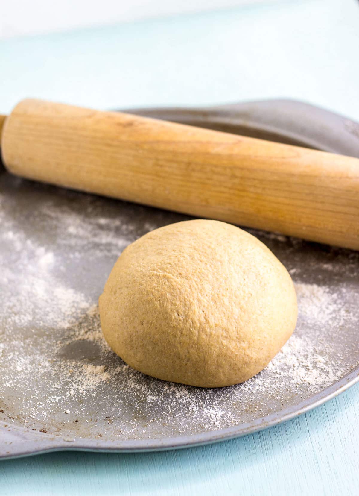 Whole Wheat Yeast Free Pizza Crust dough ball on a baking pan. There is a rolling pin sitting behind the dough.