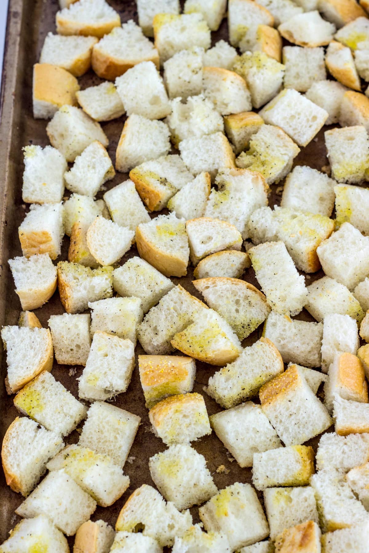Bread cubes drizzled with olive oils, salt and pepper on a baking sheet.