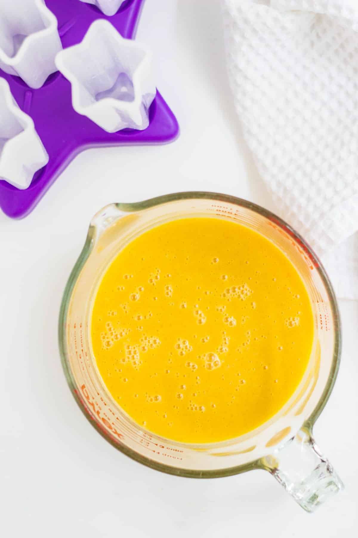 Overhead view of a measuring cup filled with blended fruit mixture.