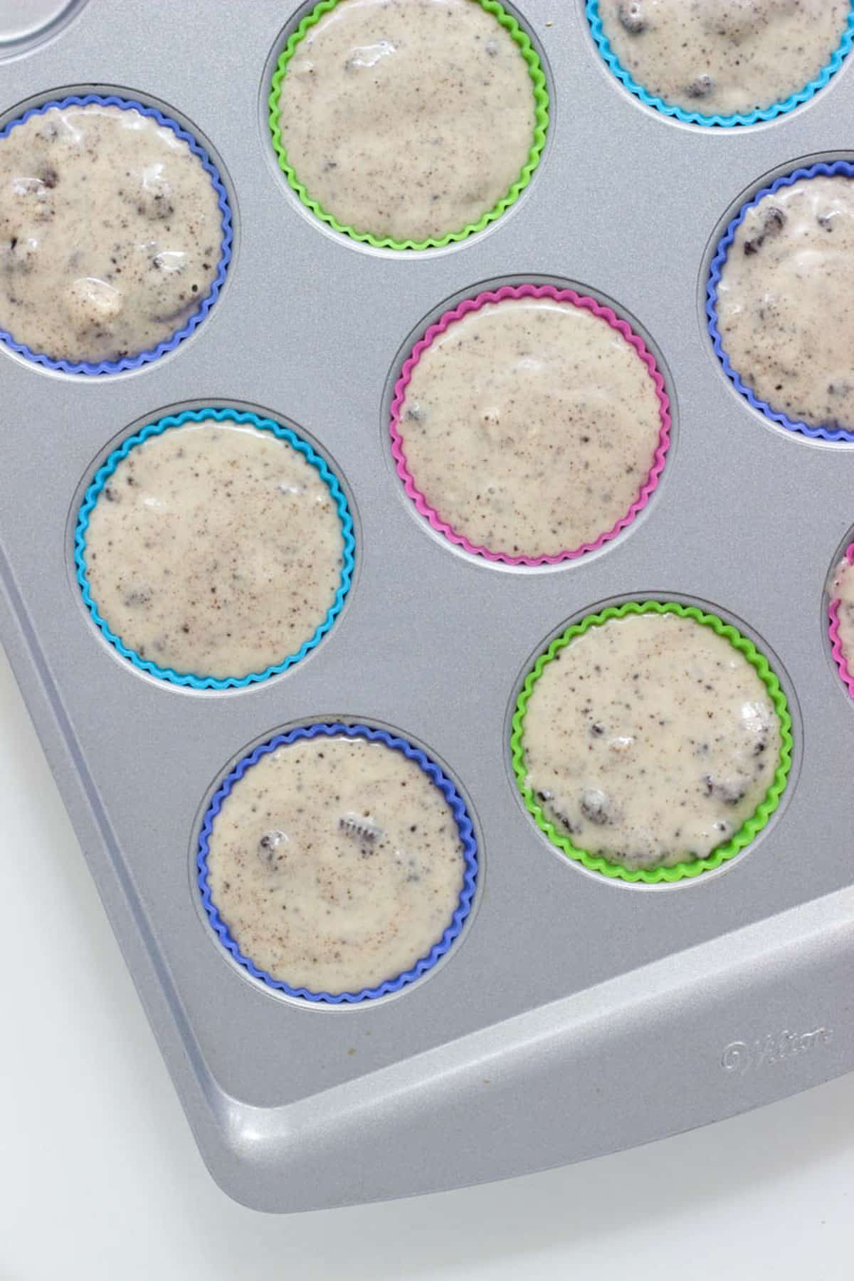 A muffin pan with colorful silicon liners filled with ice cream base before freezing.