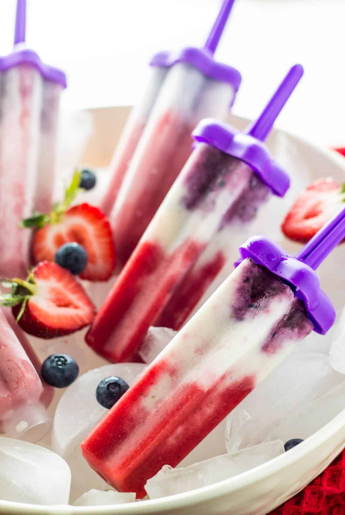 Close up of Vegan Red, White and Blue Popsicles in a bowl with ice and fresh fruit.