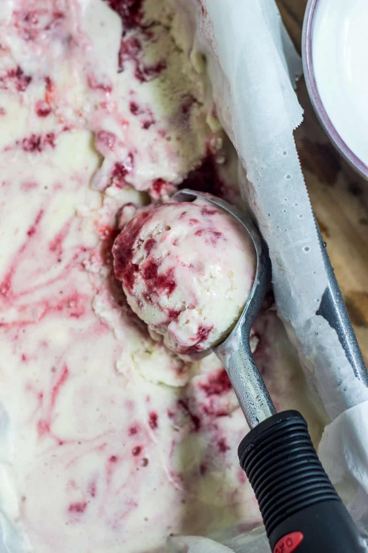 Close up of a scoop of Strawberry Swirl Coconut Ice Cream resting in dish of ice cream.