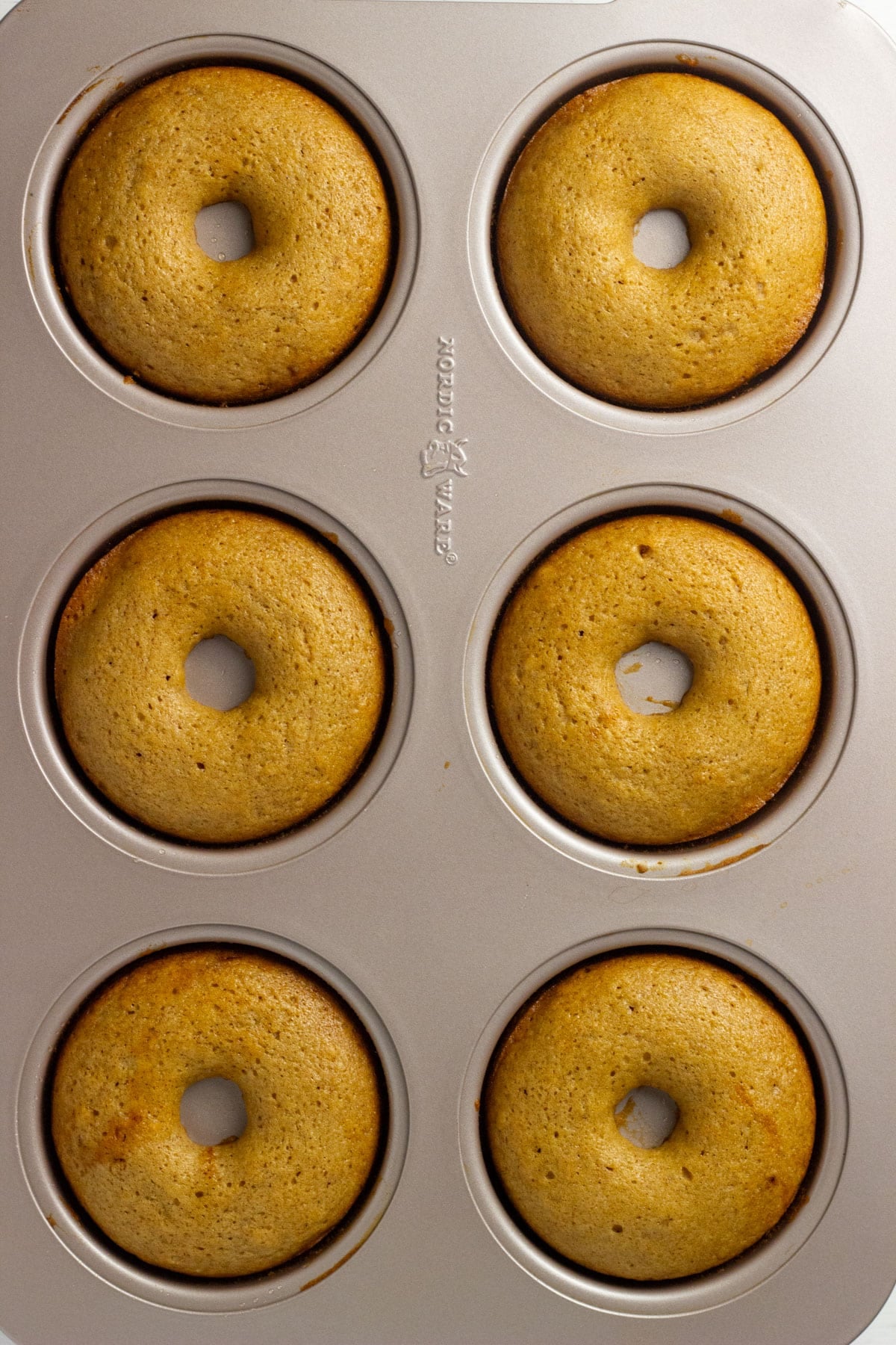Overhead view of six Vegan Apple Cider Doughnuts in a baking pan.
