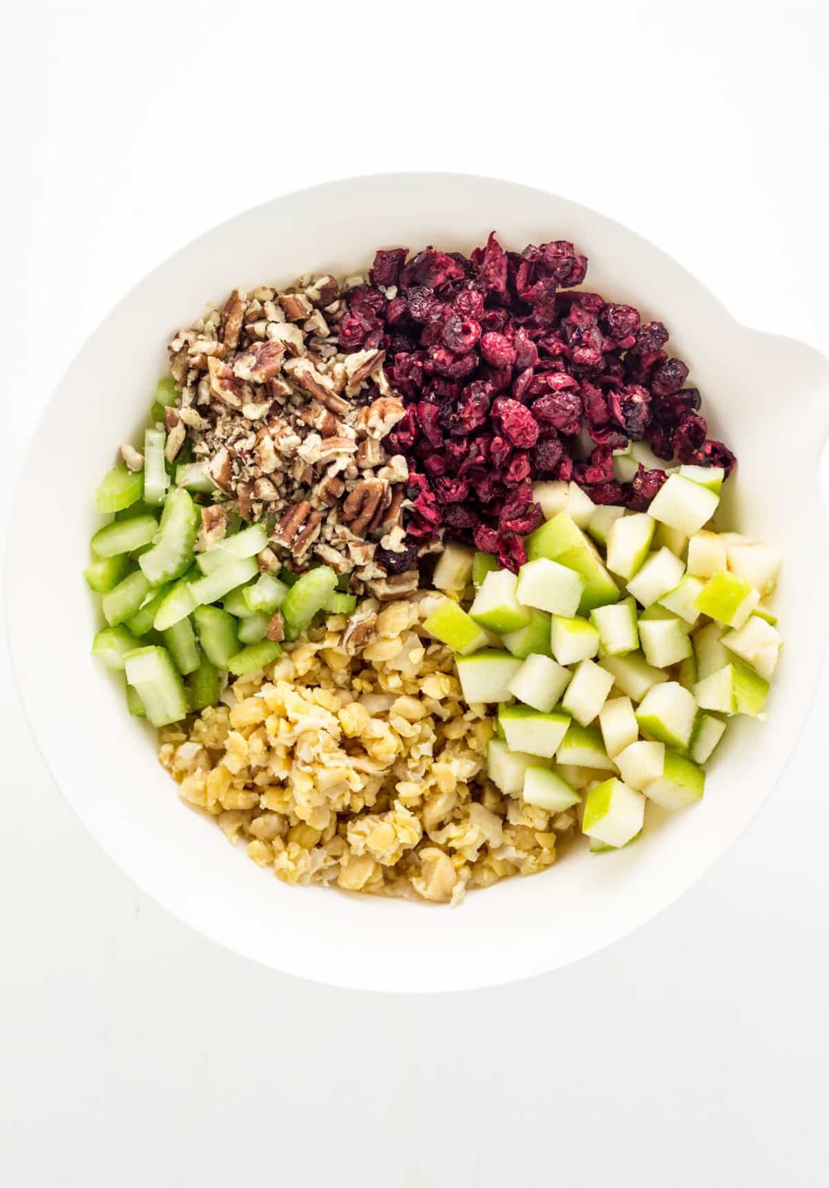 A bowl with mashed chickpeas, green apple, dried cranberries, chopped pecans and chopped celery.