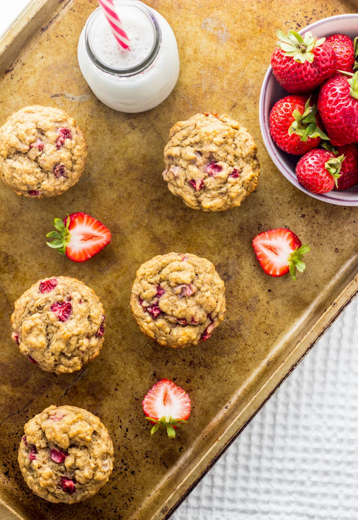 Vegan Strawberry Banana Bread Muffins on a sheet pan with fresh strawberries and a bottle of non dairy milk.