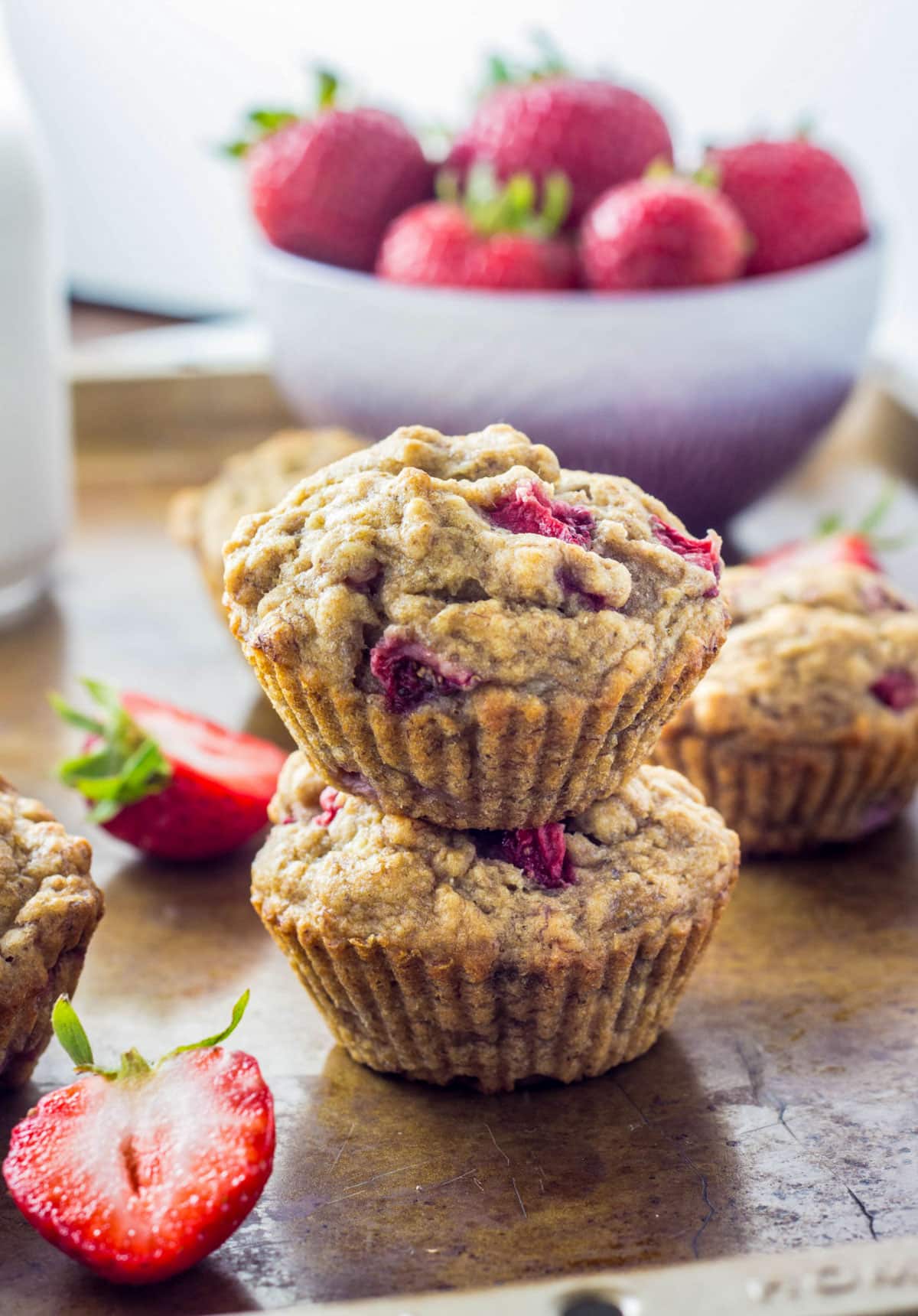Two Vegan Strawberry Banana Bread Muffins stacked. There is a bowl of strawberries in the background.