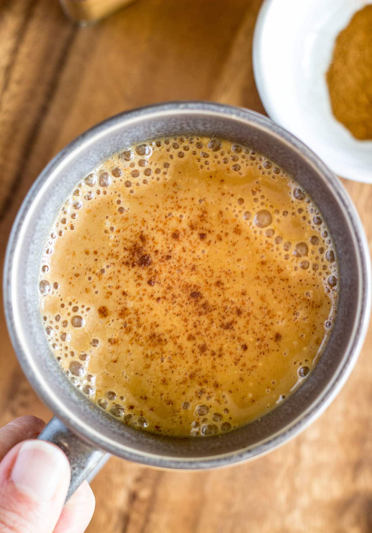 Overhead shot of Vegan Warm Spiced Pumpkin Milk in a grey mug with a hand holding the handle.
