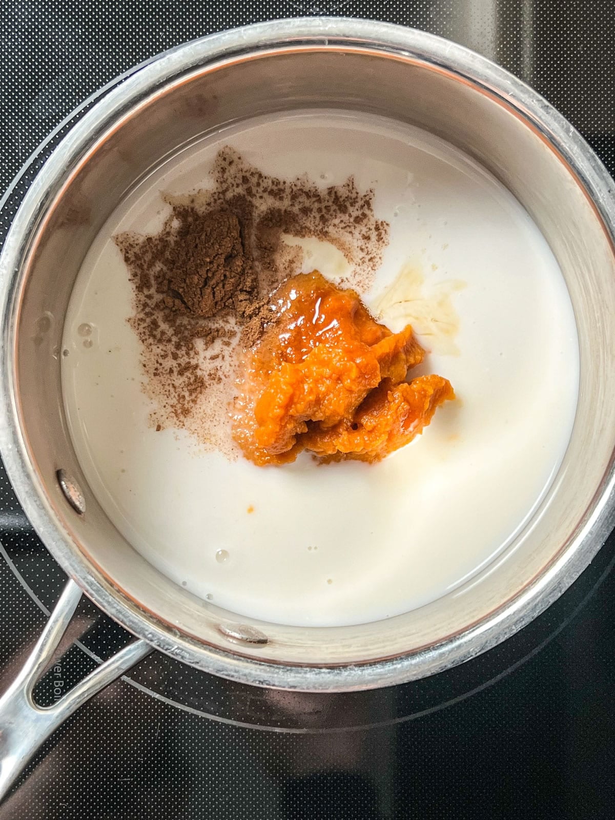 Overhead shot of non dairy milk, pumpkin puree, maple syrup and salt in sauce pan.