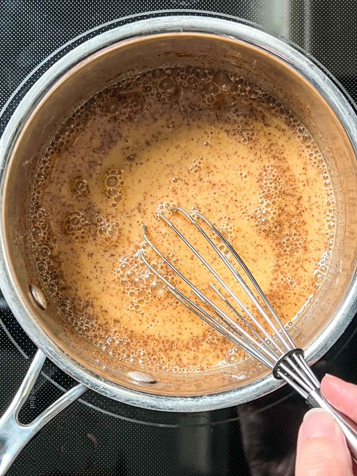 Overhead shot of pumpkin milk in saucepan with whisk.