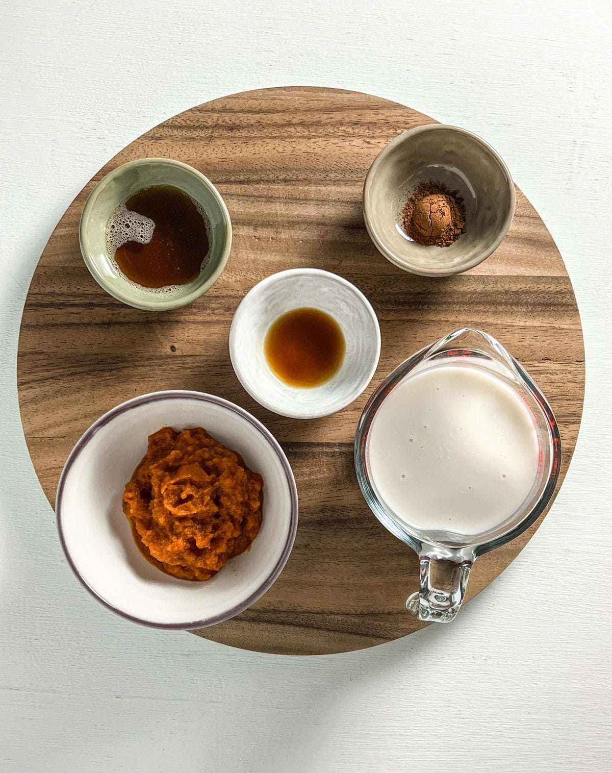 Overhead shot of ingredients for Vegan Warm Spiced Pumpkin Milk. There is non dairy milk, pumpkin puree, maple syrup, pumpkin pie spice and vanilla.