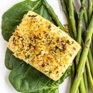 Top view of Baked Lemon & Herb Crusted Tofu on a bed of spinach and a side of asparagus on a white plate