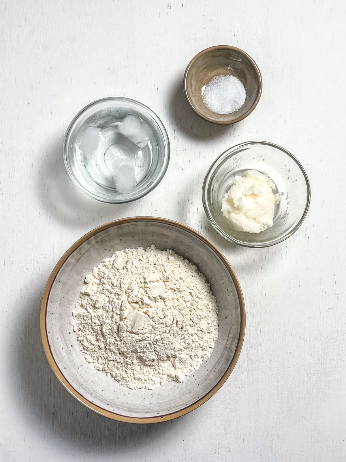 Ingredients for Coconut Oil Pie Crust. There is a bowl of spelt flour, firm coconut oil, salt and ice water.