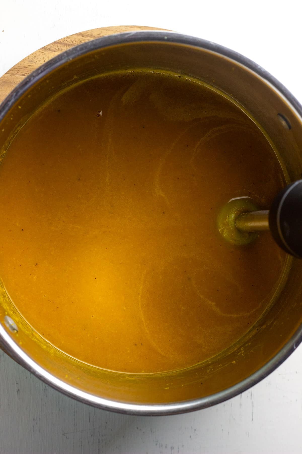 Close up of a pot of squash soup with an immersion blender.
