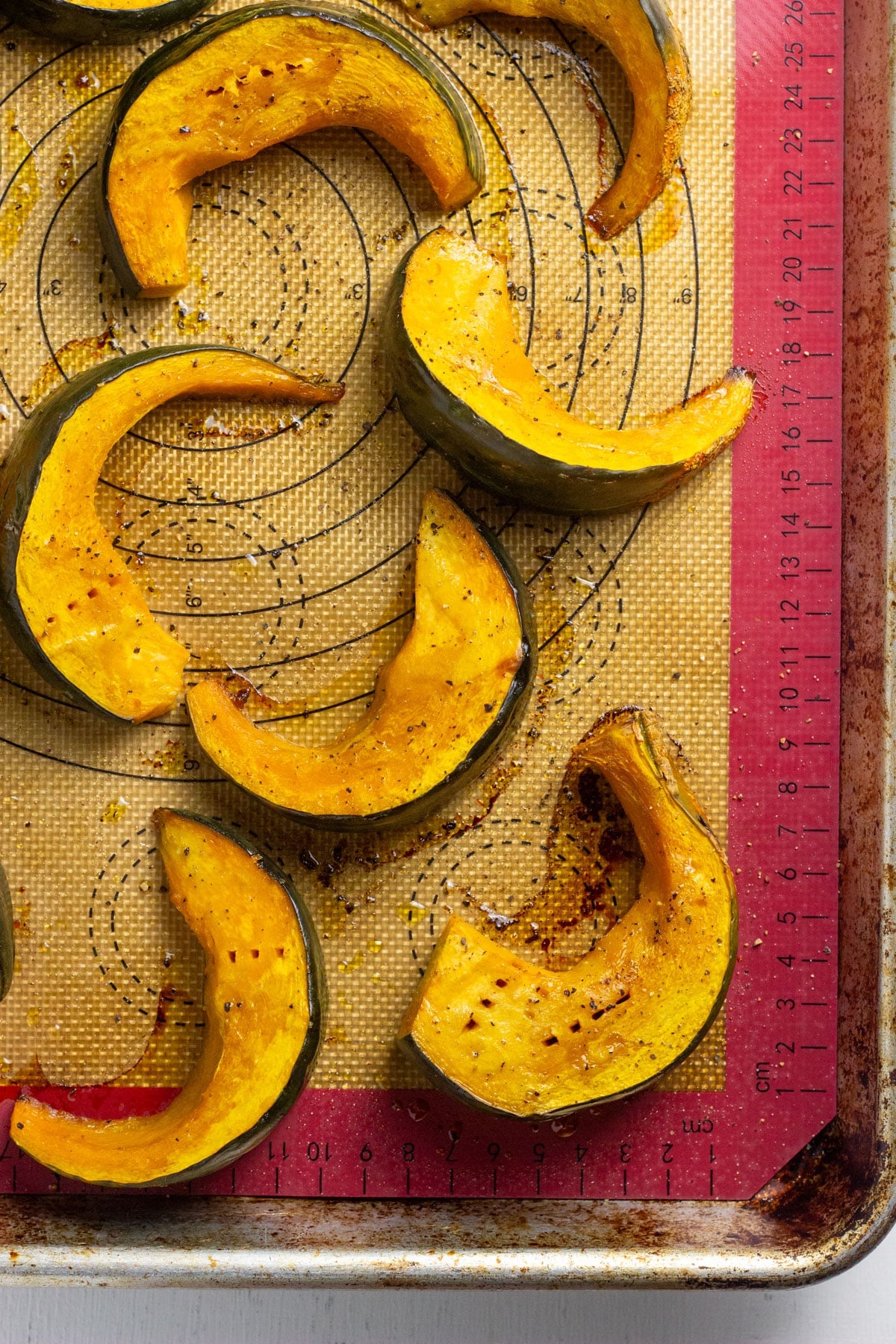 Overhead view of wedges of roasted squash on a baking sheet lined with a silicone mat.