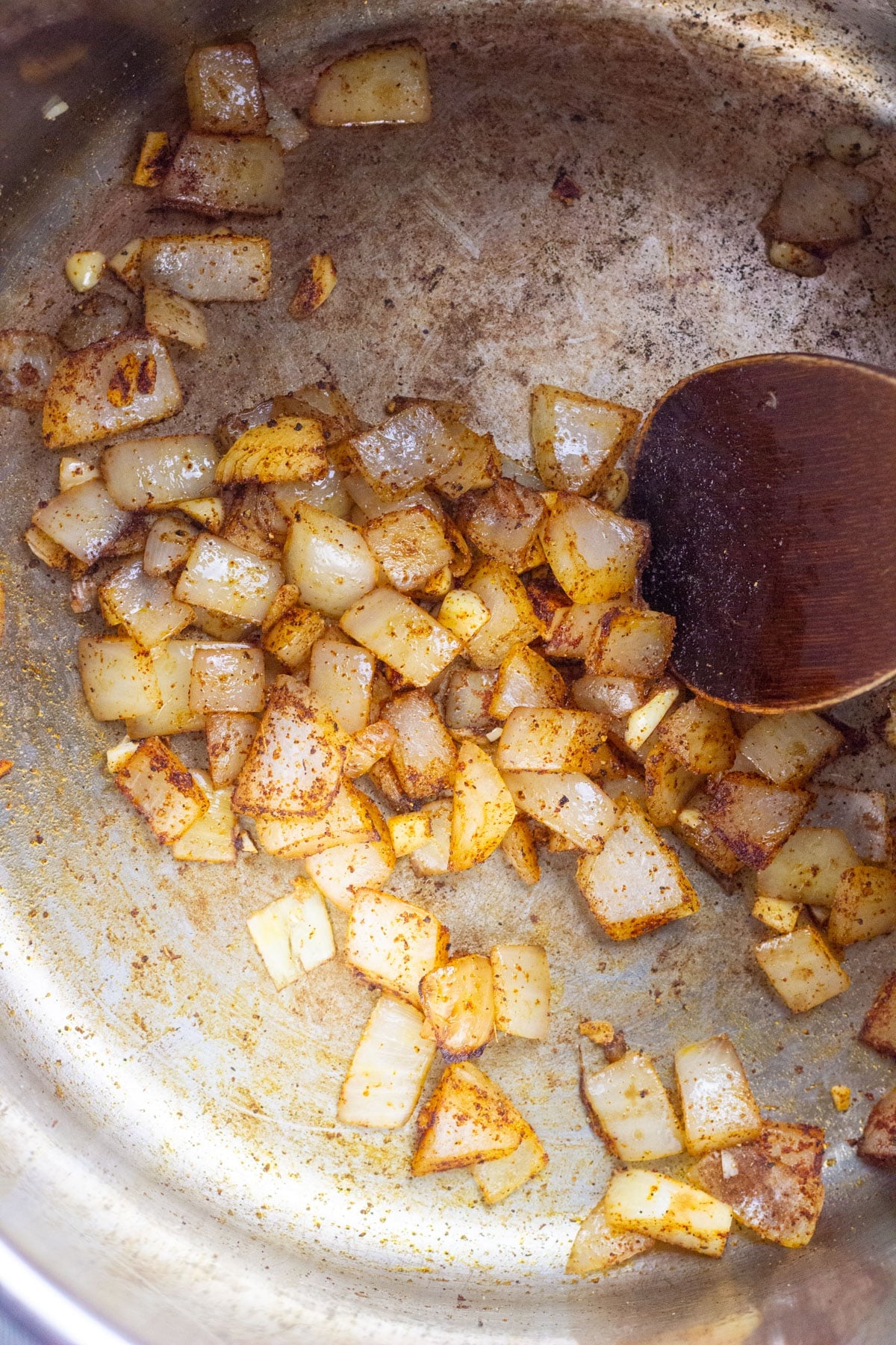 Close up of chopped onions and spices in a stainless steel pot.
