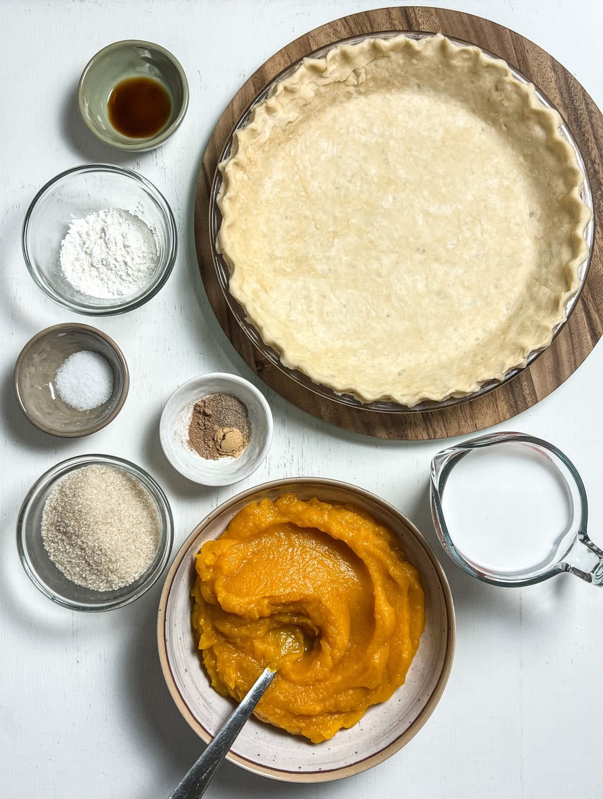 Bowls of pumpkin puree, coconut milk, pie crust, cane sugar, salt, spices, cornstarch and vanilla. These ingredients will make a vegan Cardamom Pumpkin Pie.