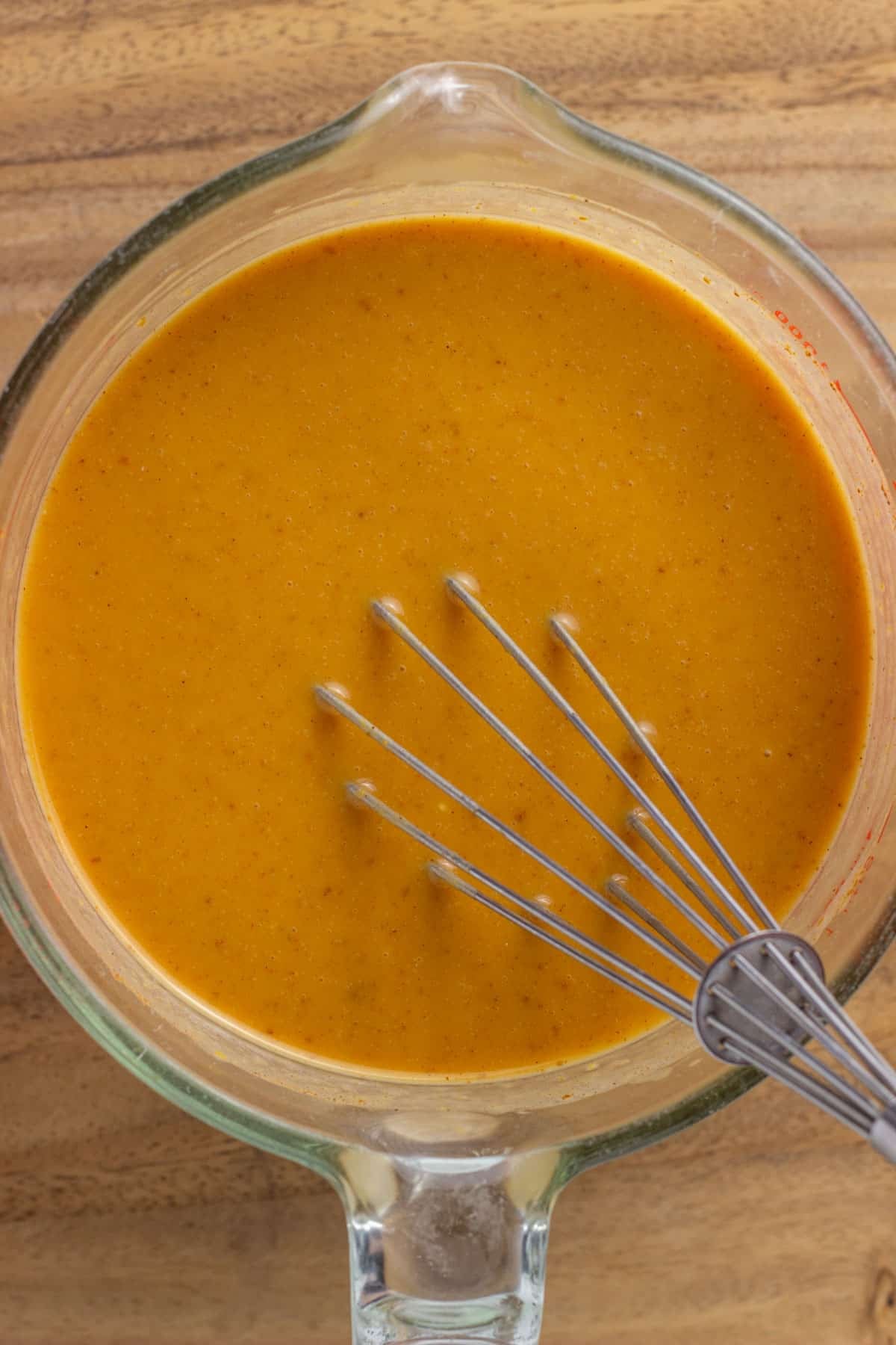 A measuring cup with the base for making Vegan Pumpkin Ice Cream. A whisk is in the cup.