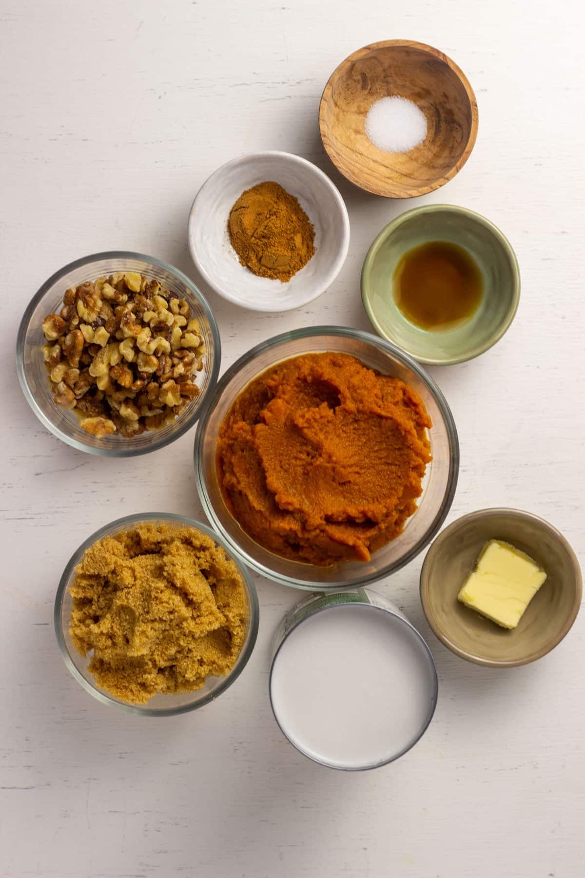Bowls of ingredients to make ice cream including pumpkin puree, coconut milk, brown sugar, vanilla, pumpkin pie spice, salt, walnuts and vegan butter.
